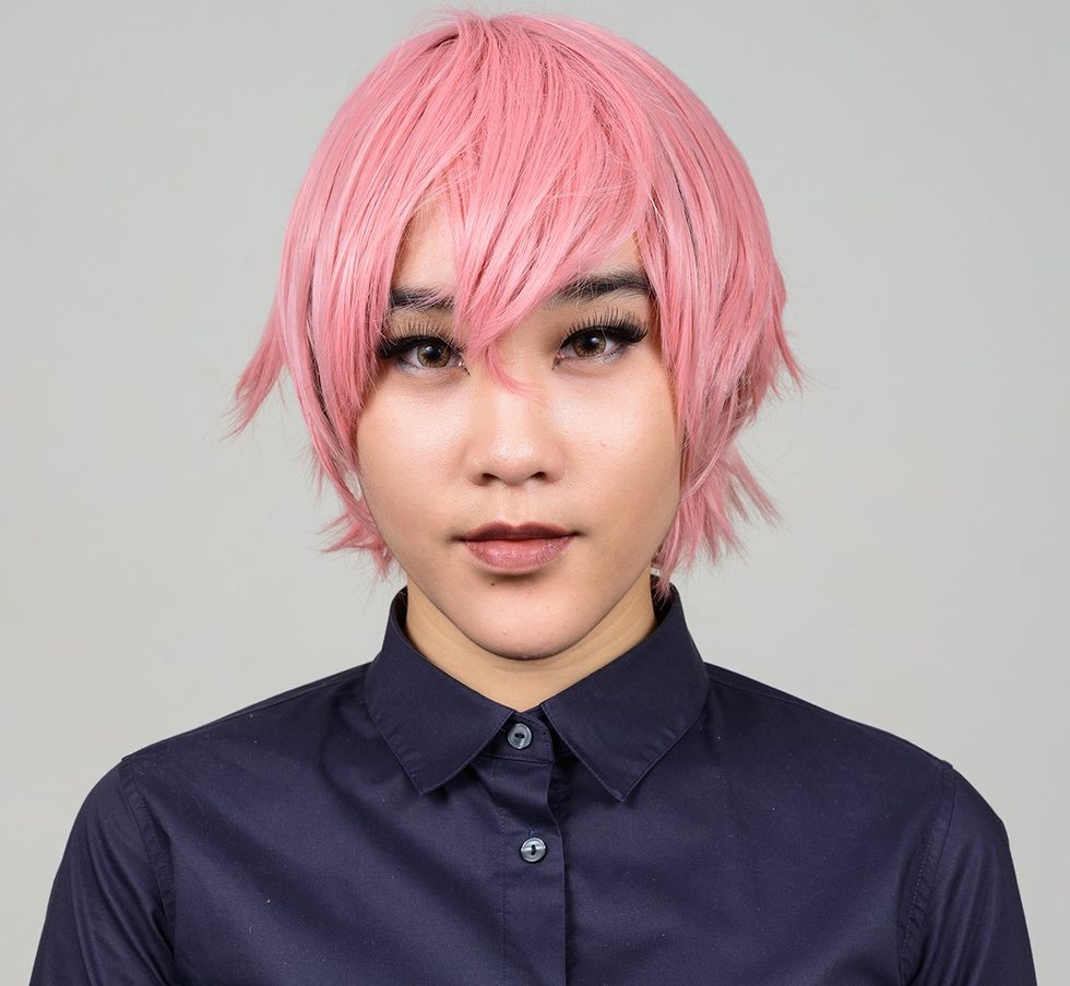 transgender person in pink wig with blue shirt neutral gray background