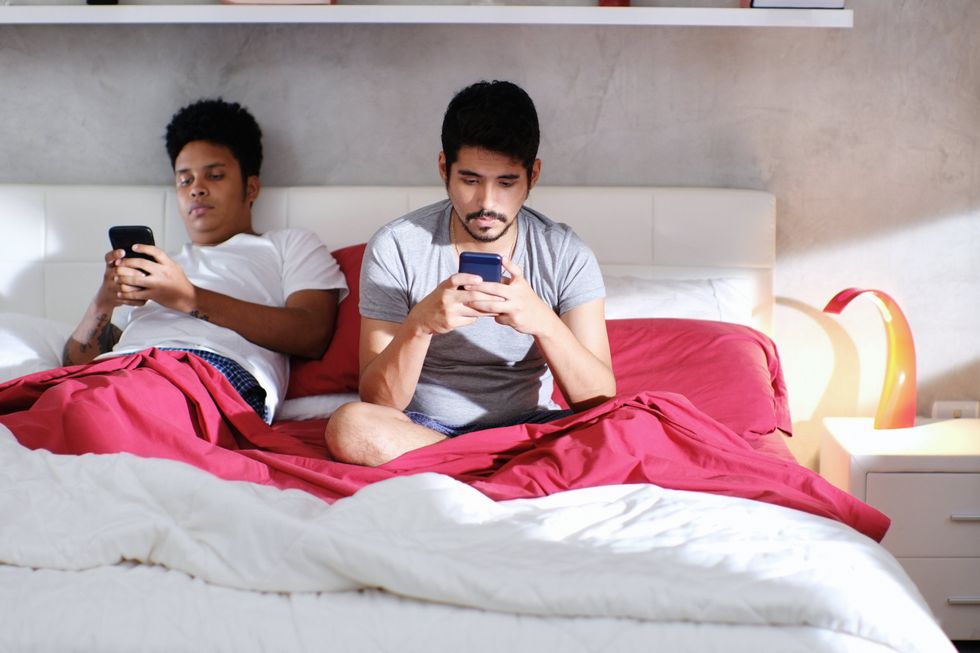 two clothed men on their phones in bed