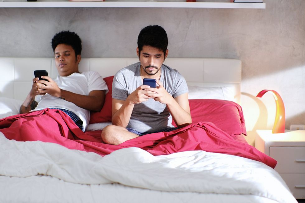 two clothed men on their phones in bed