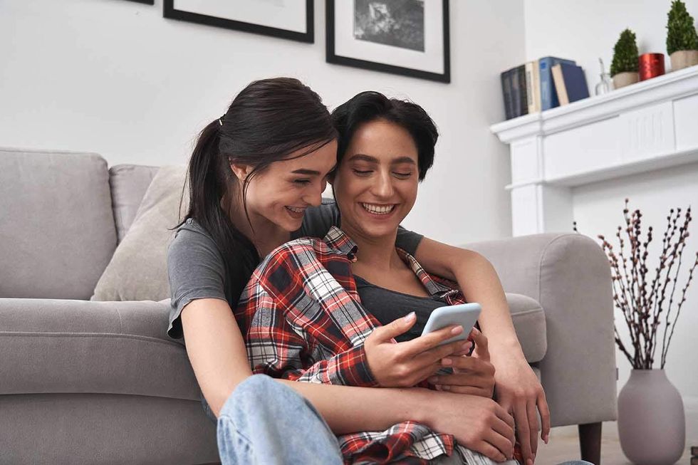 Two lesbians embracing with one holding a cell phone