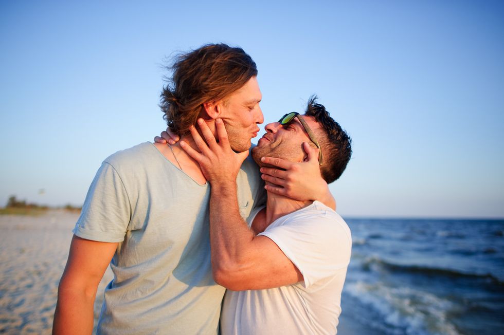 Two men embrace against the background of the sea. They represent a playful kiss.