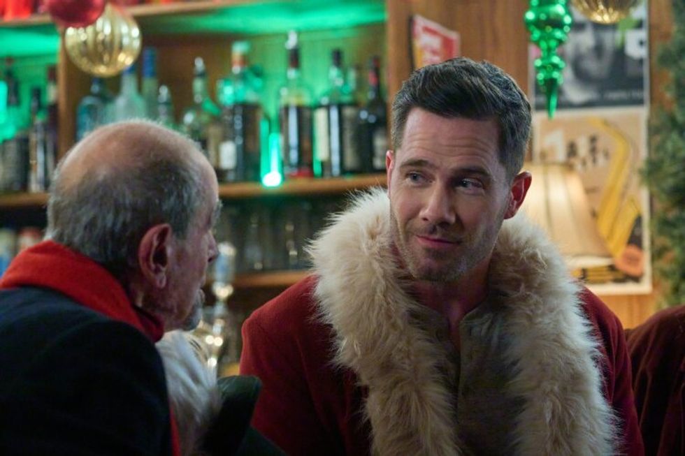 Two men have a conversation in a bar and one is wearing a Santa coat.