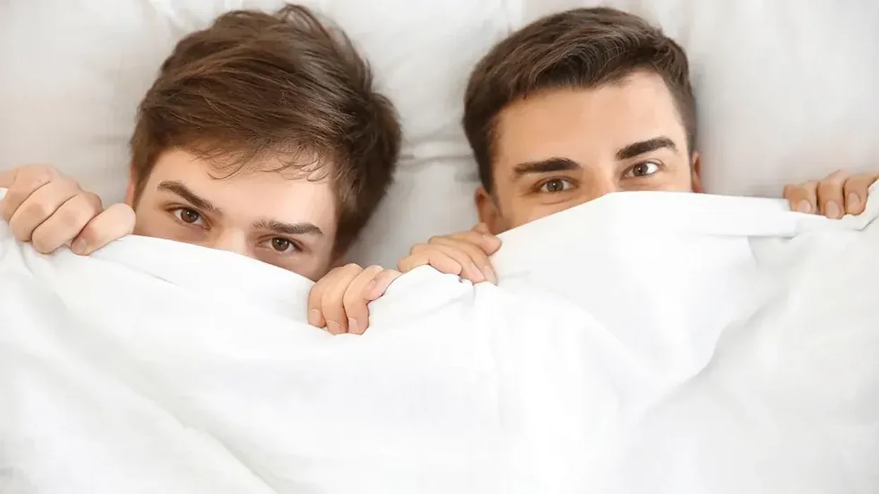 two men in bed pulling a sheet over their face