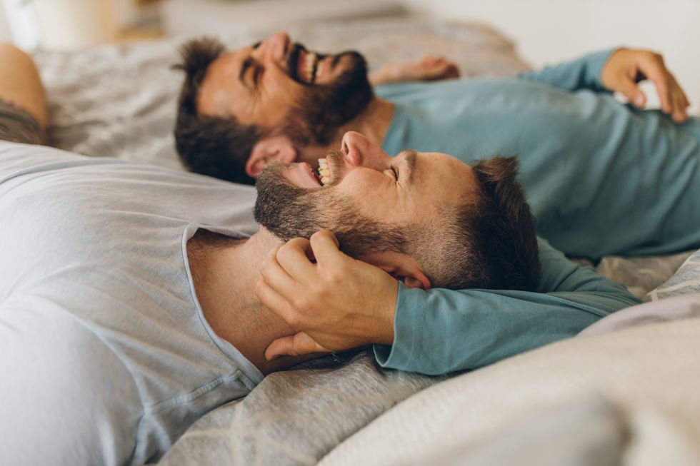 two men laughing in bed
