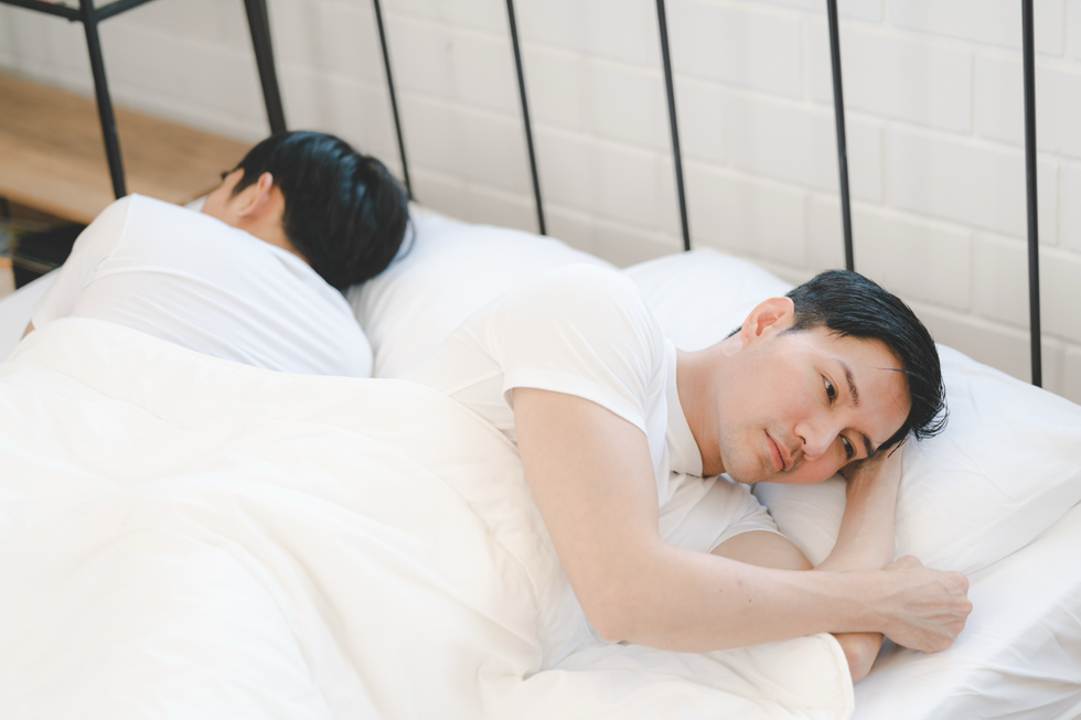 Two men laying in bed together, facing opposite directions.