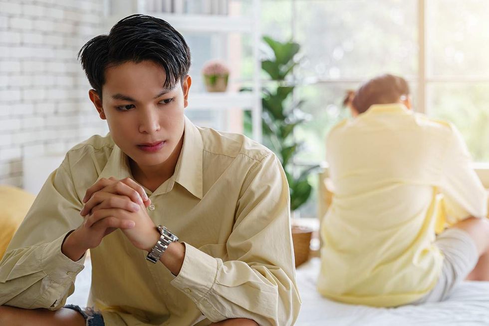 Two men sitting on a bed ignoring each other