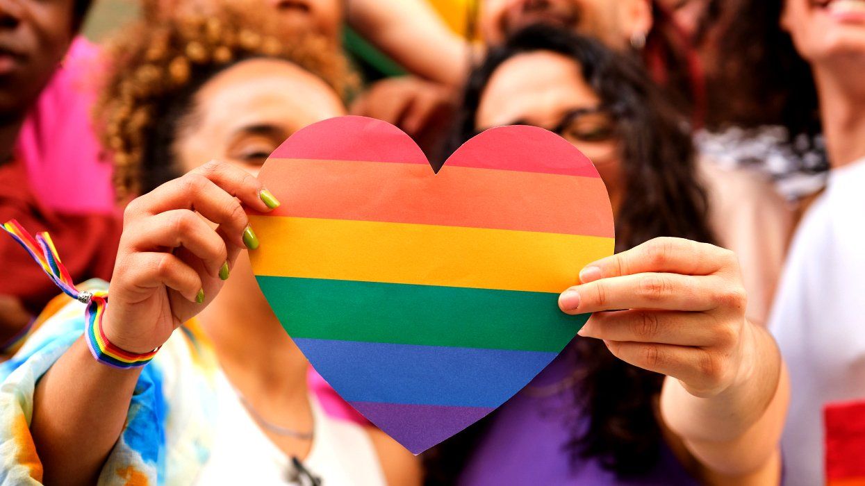 two women lesbian couple holding rainbow paper heart surrounded by happy LGBTQIA community