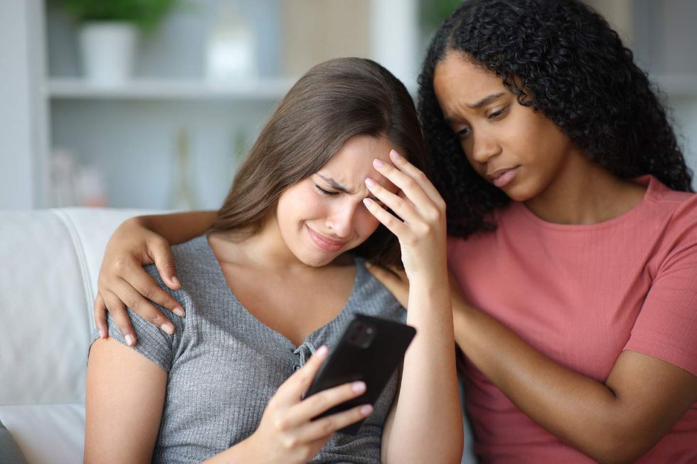 Woman upset while looking at her cell phone and another woman comforts her