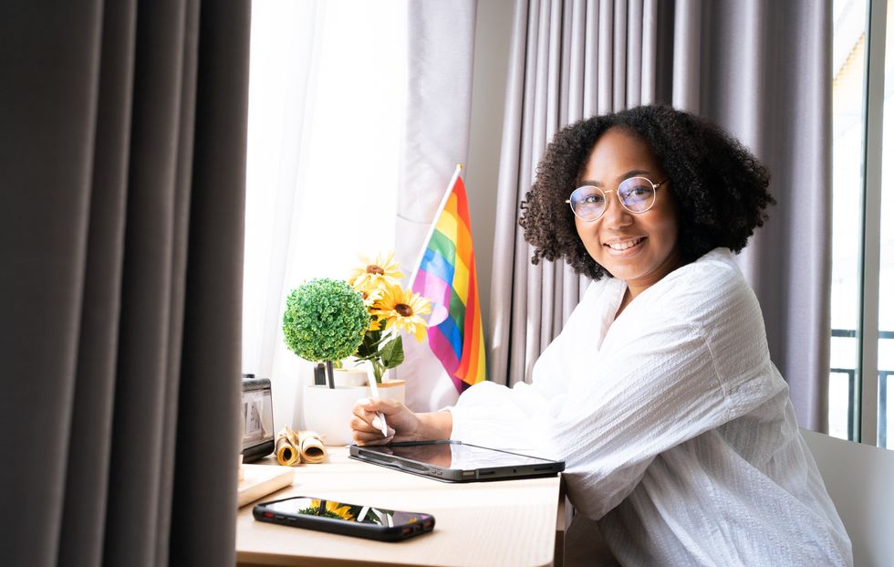Working woman LGBTQ+ Afro hair style African American lesbian, Beautiful gay working on tablet with love moment spending good time together, lgbt rainbow, pride flag on table near curtain at window.