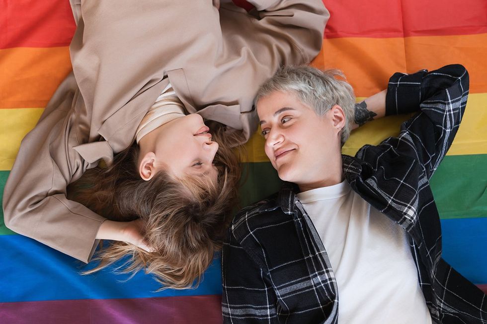 Young females lesbians LGBT couple lying on the rainbow flag looking at each other with love and passion for equality and sexual minorities rights. Transgender couple protesting for freedom in love