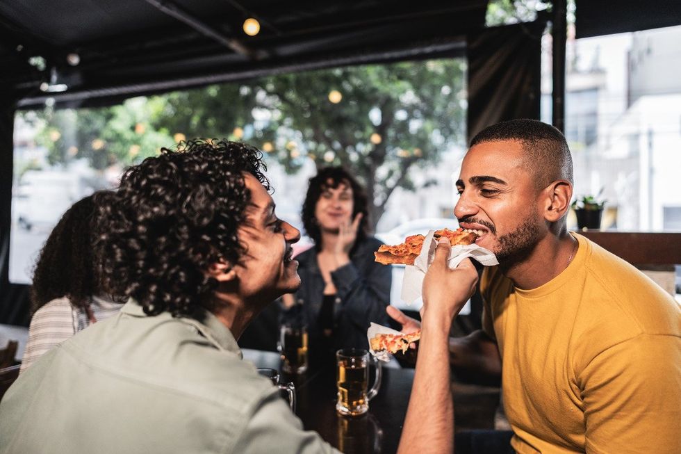Young gay man giving a slice of pizza for boyfriend at restaurant