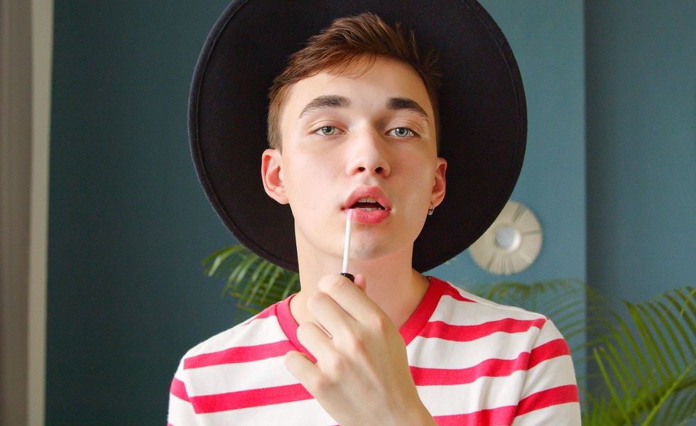 Young man holding lipstick or lip gloss and paints lips prepare getting ready