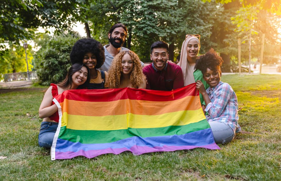 Young multiracial people taking a group photo holding an LGBT rainbow flag in the park