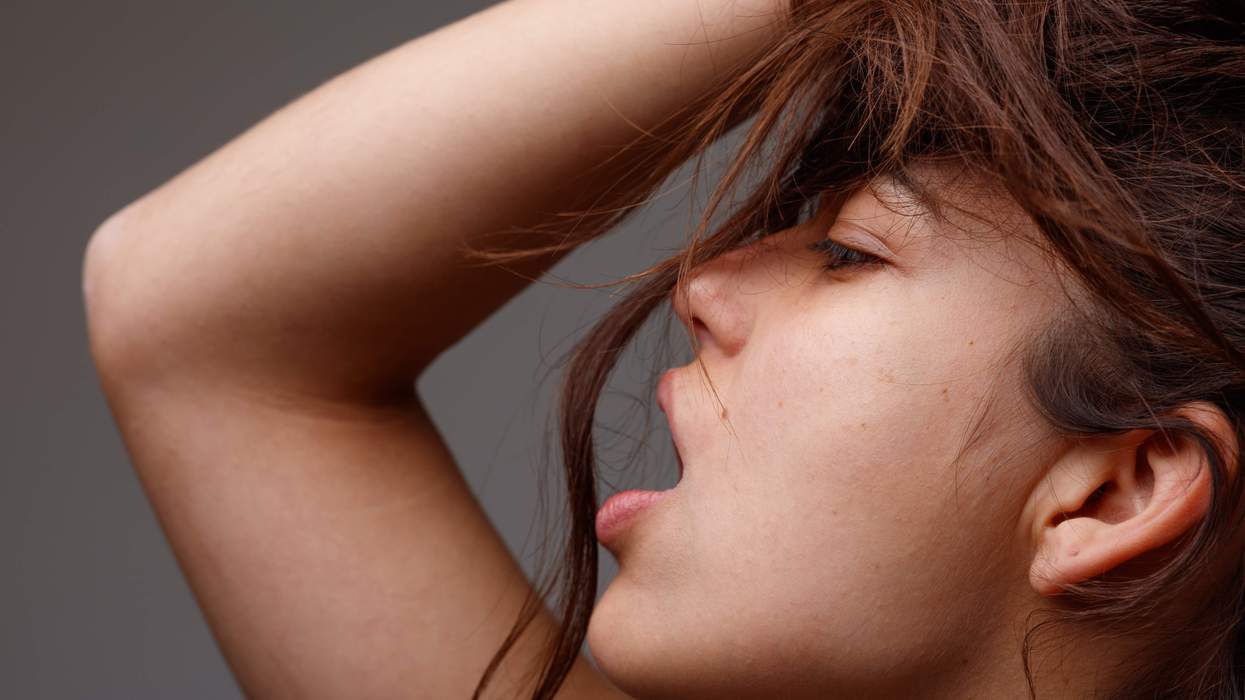 young woman posing with mouth open and hand raised to her tousled long brown hair