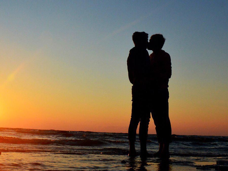 A photo of a gay couple kissing on the beach. 